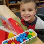 Ayden using assorted colored buttons to match colors on pegboard to make pictures